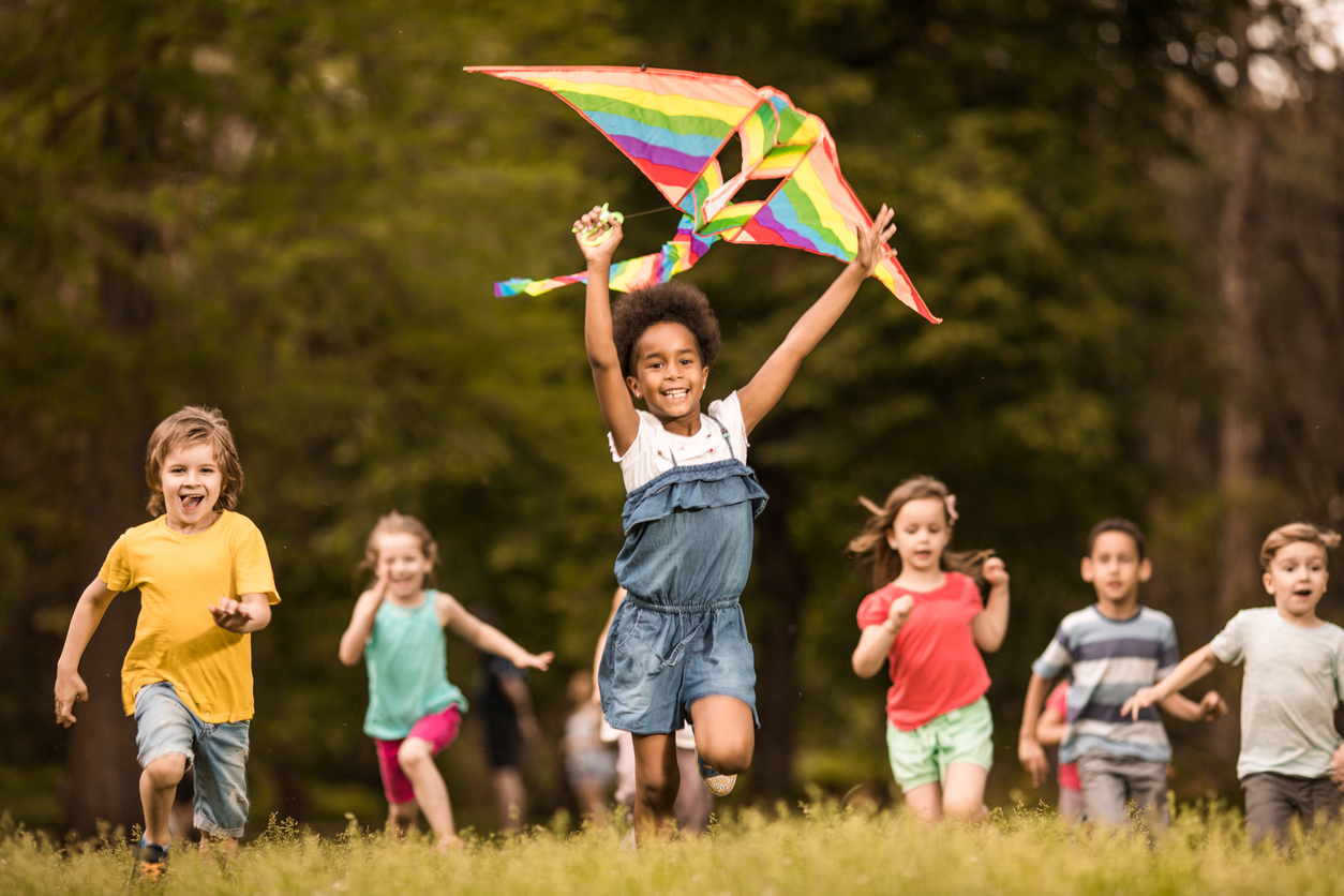 Group of happy kids having fun while running with a kite at the park. 